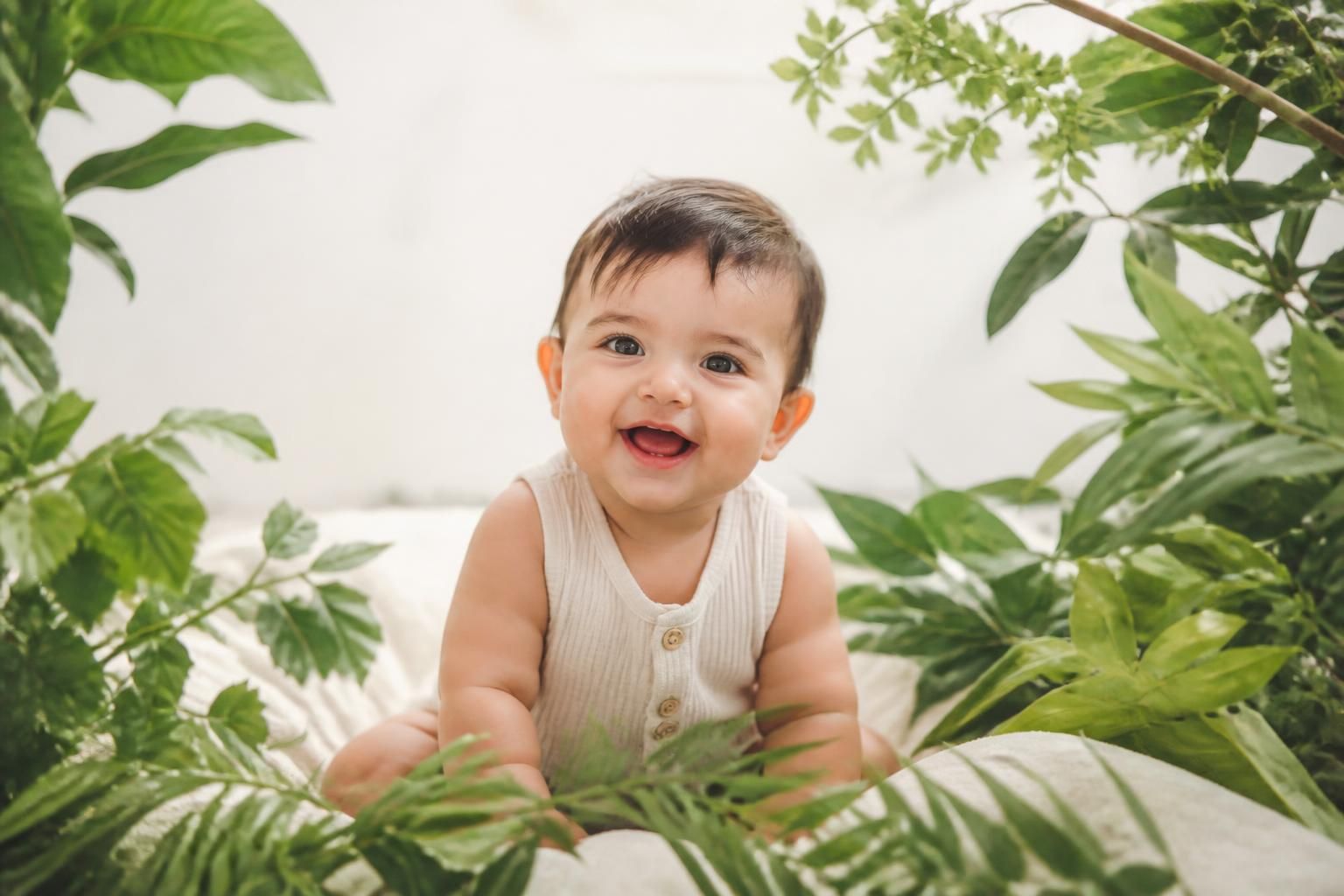 Happy baby surrounded by lush green leaves in a bright