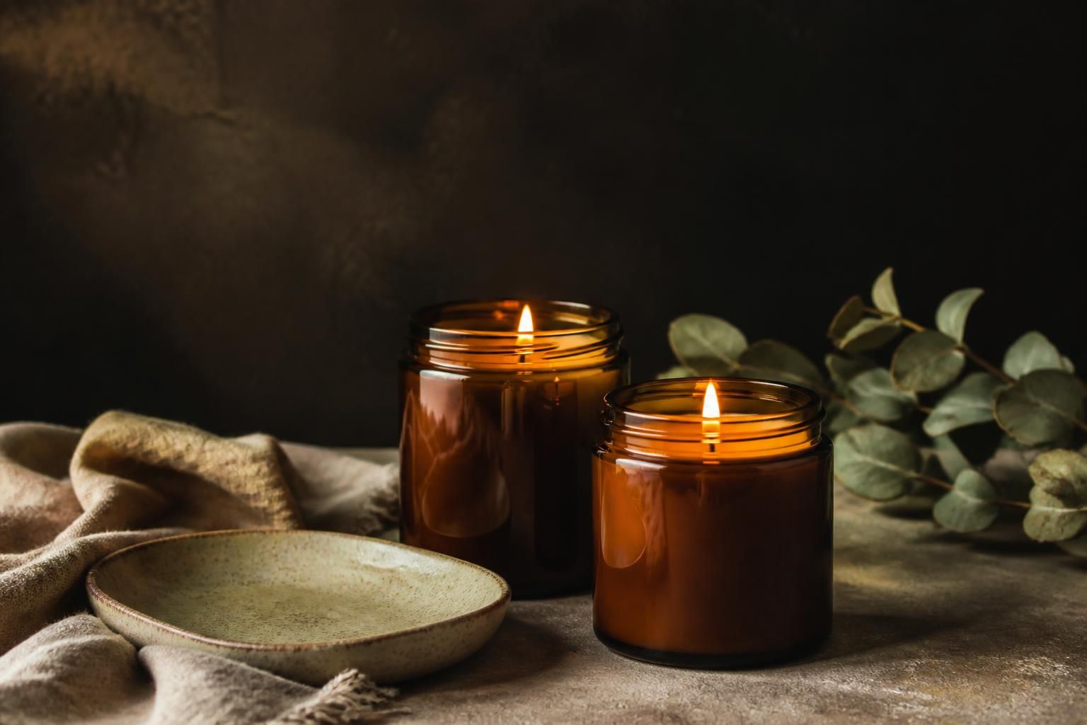 A pair of hand-poured soy candles in refillable jars beside a ceramic tray and folded neutral fabric
