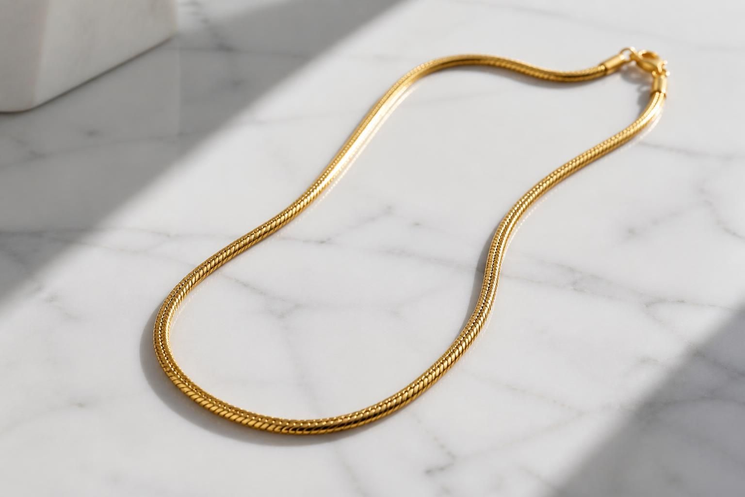 A premium GOLDAS men’s snake chain necklace laid on a clean white marble surface with soft natural window light